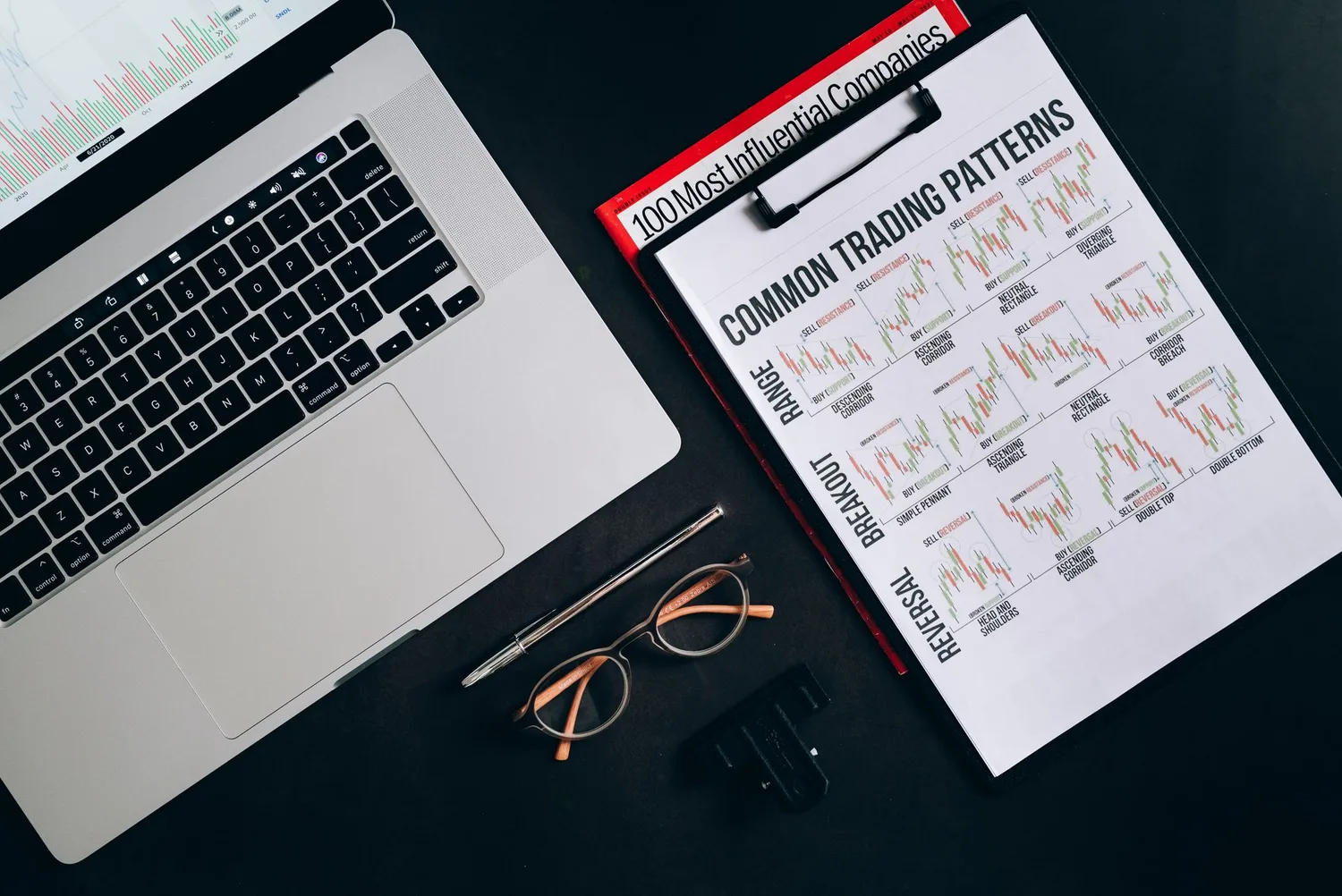 Espacio de trabajo financiero oscuro con portátil, gráficos impresos y herramientas de análisis.